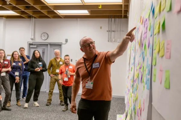 Trace facilitating a group conversation beside a wall of participant notes
